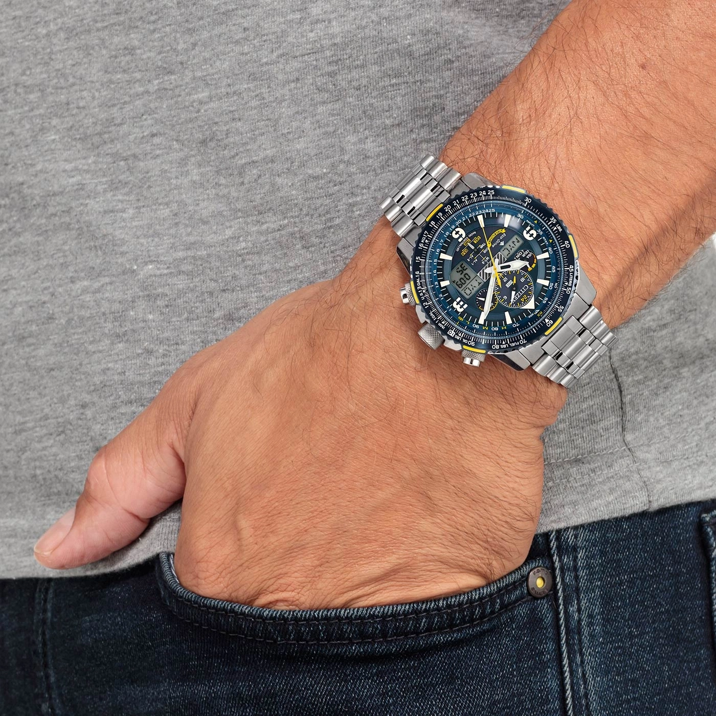 Mann mit Citizen-Uhr, Hand in der Tasche, graues Hemd, blaue Jeans.