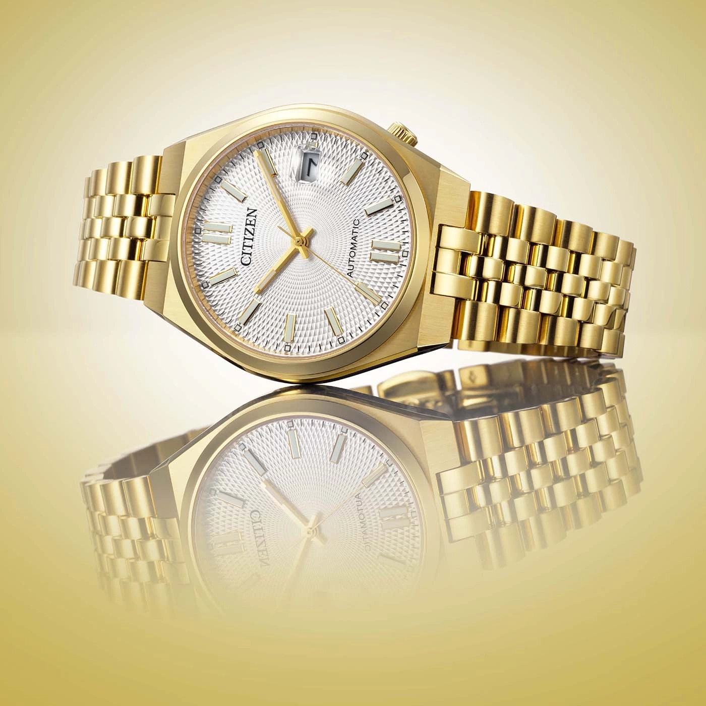 Eine Nahaufnahme im Studio eines luxuriösen goldenen Citizen Automatik-Uhr mit weißem Zifferblatt und passendem Armband, reflektiert auf goldener Oberfläche.