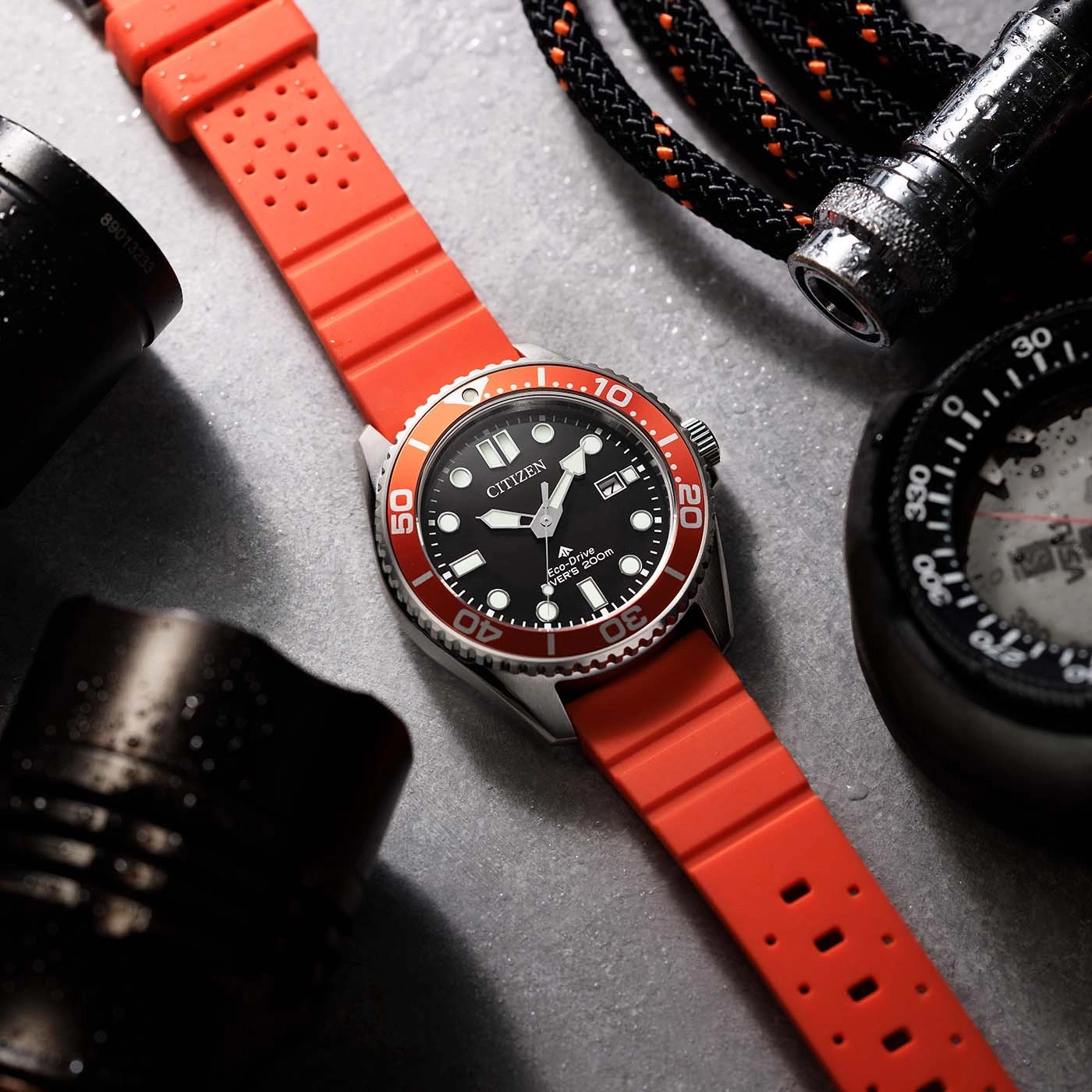 Nahaufnahme einer Citizen Eco-Drive Taucheruhr mit rotem Band, neben einem Kompass und einer Taschenlampe.