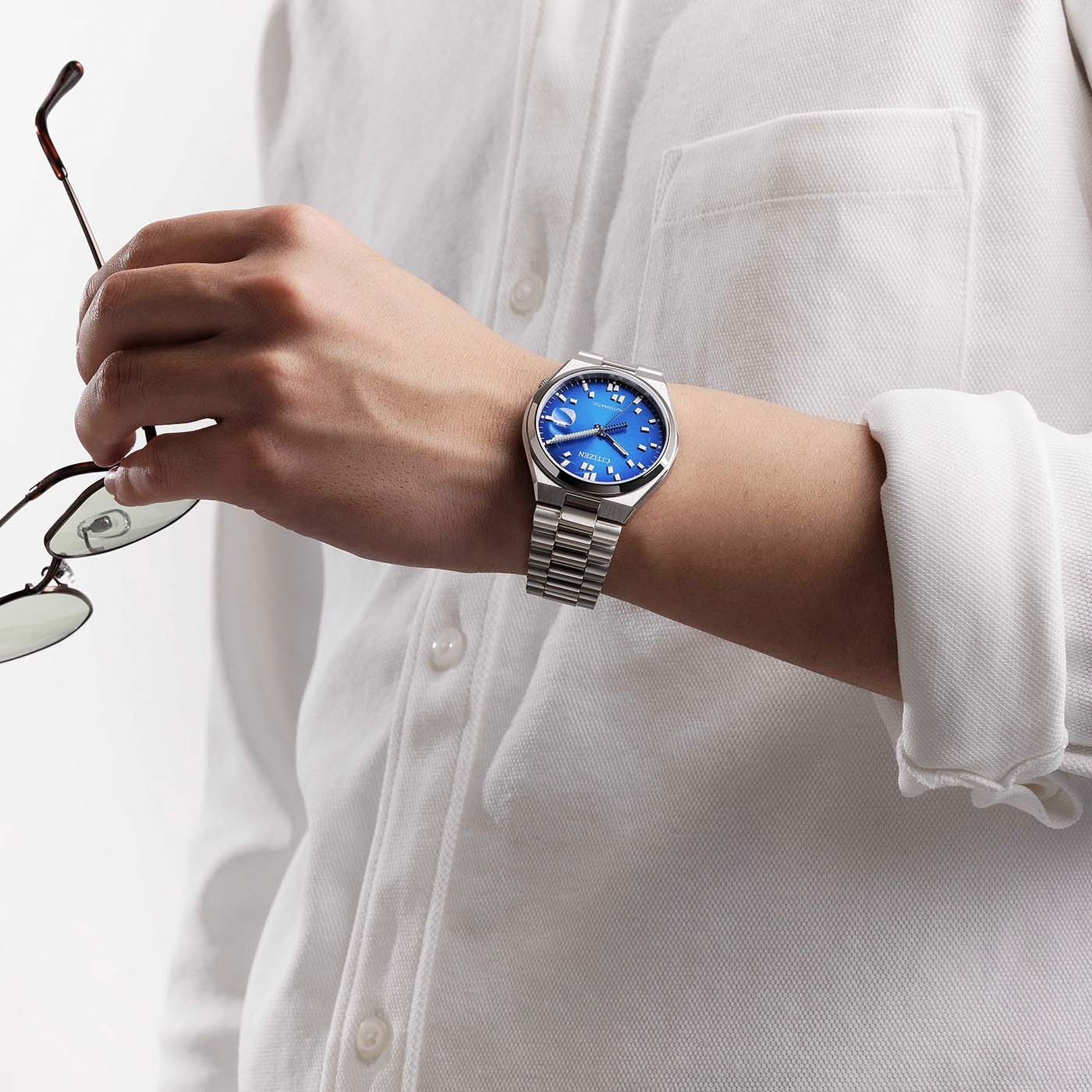 Mann im weißen Hemd mit blauer Uhr, hält Brille.