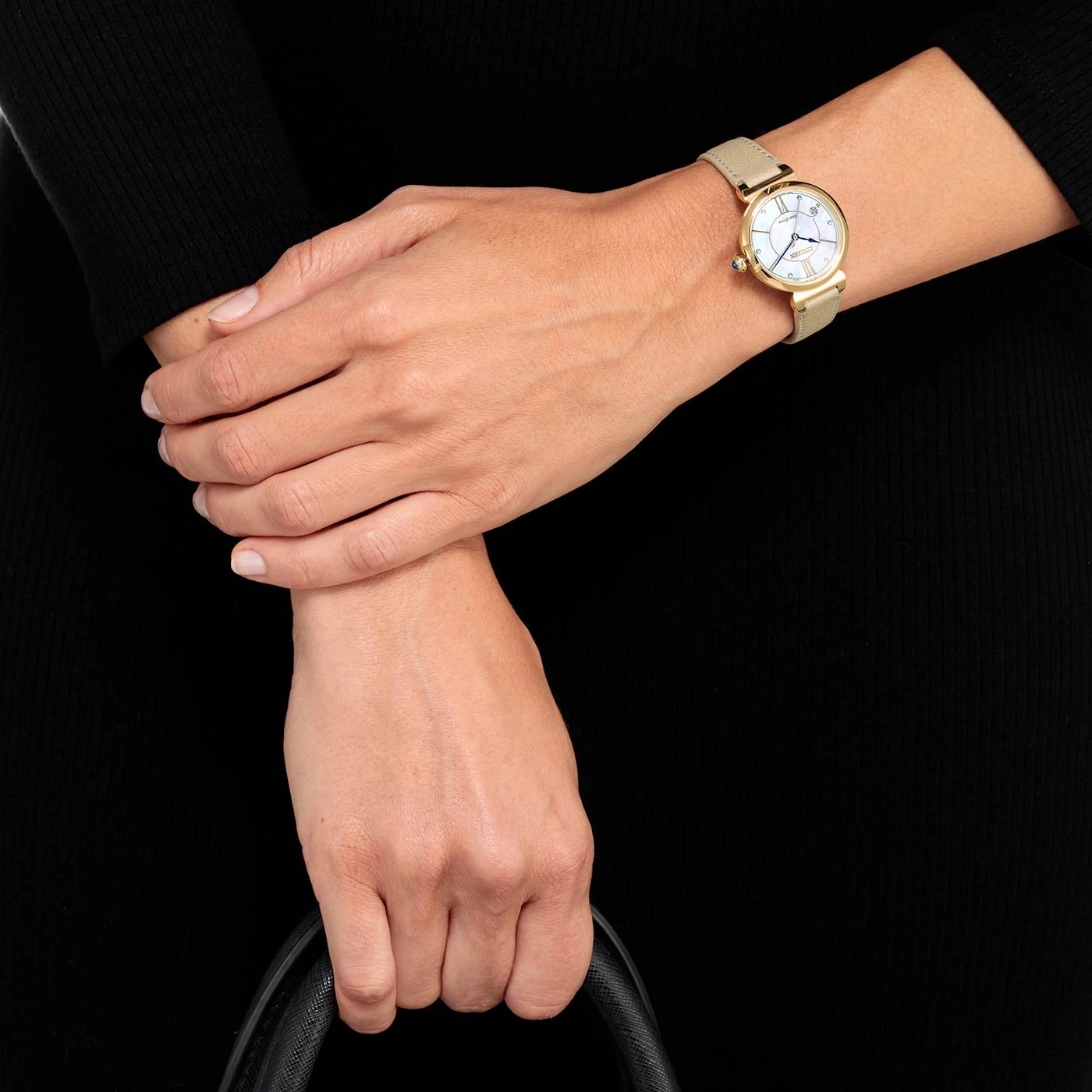 Frau mit goldener Uhr, hält schwarze Tasche, schwarzes Kleid