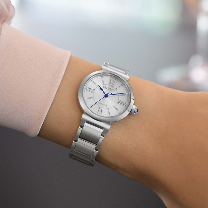 Eine Frau trägt eine silberne Citizen Eco-Drive Uhr mit römischem Zifferblatt.