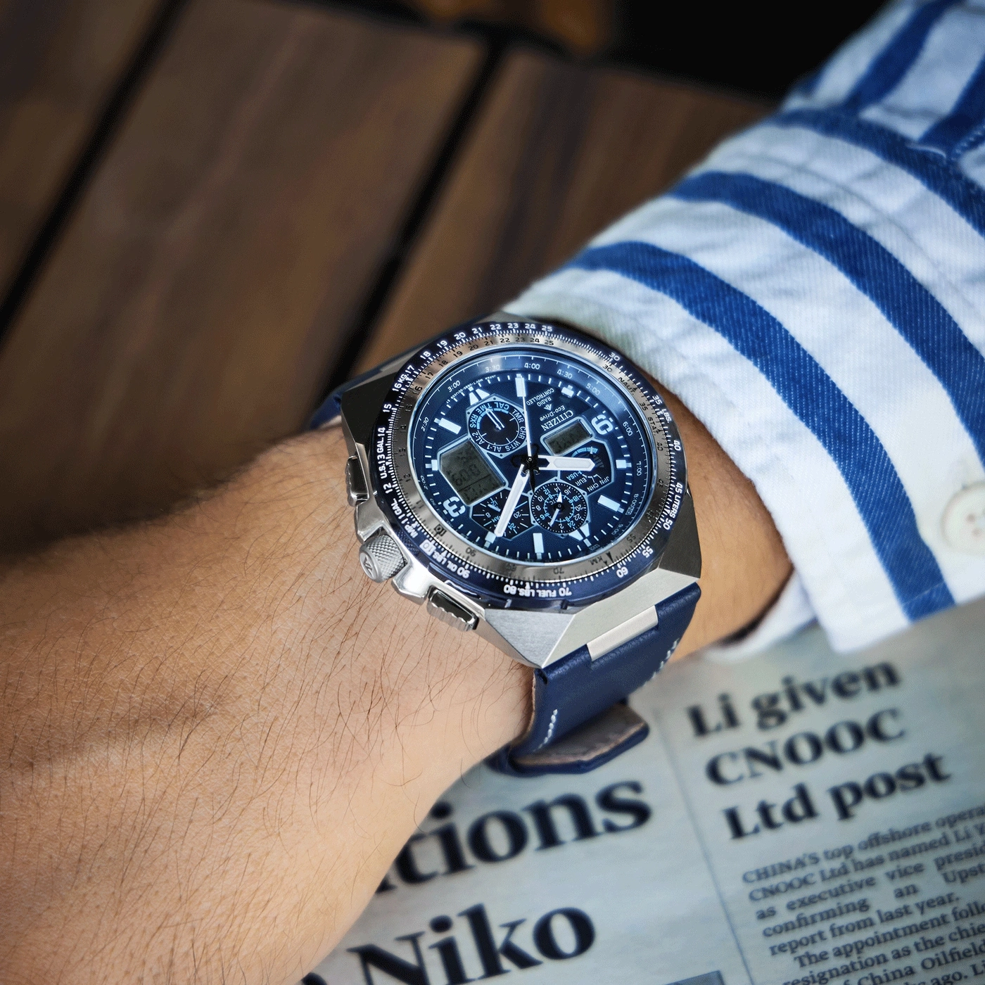 Armbanduhr mit blauem Armband am Arm einer Person, Zeitung im Hintergrund.