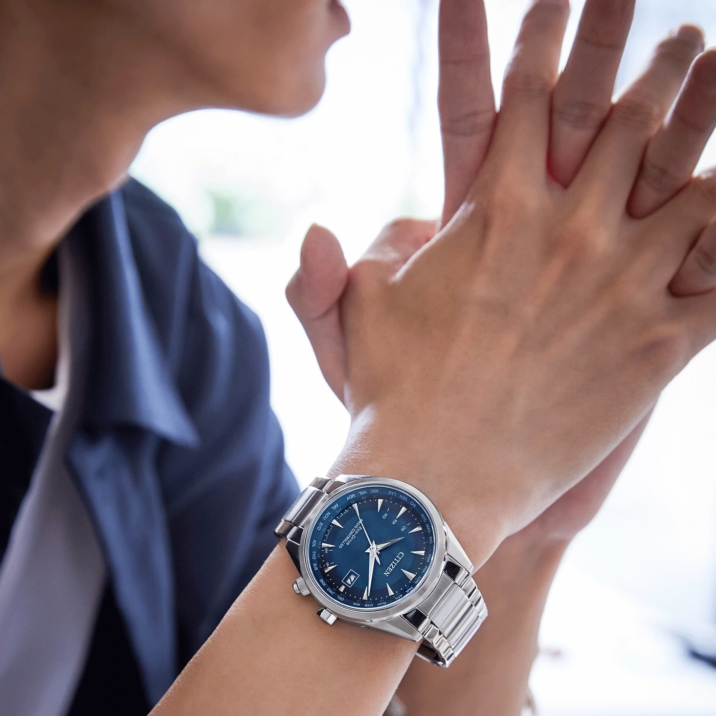 Person trägt eine Citizen-Uhr mit blauem Zifferblatt und silbernem Armband.