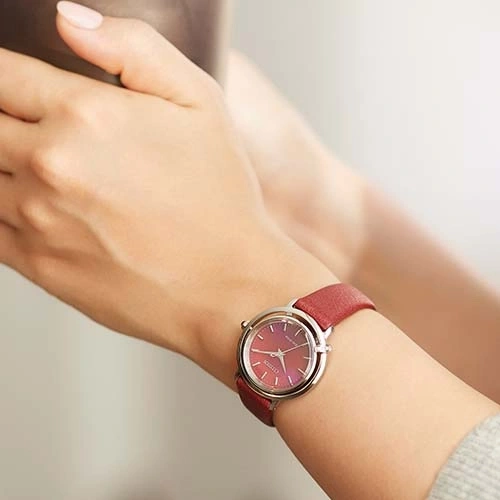 Ein rotes Armbanduhr an einem Handgelenk. Die Uhr hat ein rotes Armband und ein silbernes Gehäuse.