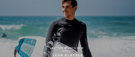 Mann im Neoprenanzug mit Surfbrett am Strand, lächelnd, Interview.