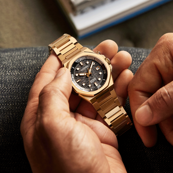 Nahaufnahme einer goldenen Citizen-Uhr, die von den Händen einer Person gehalten wird.