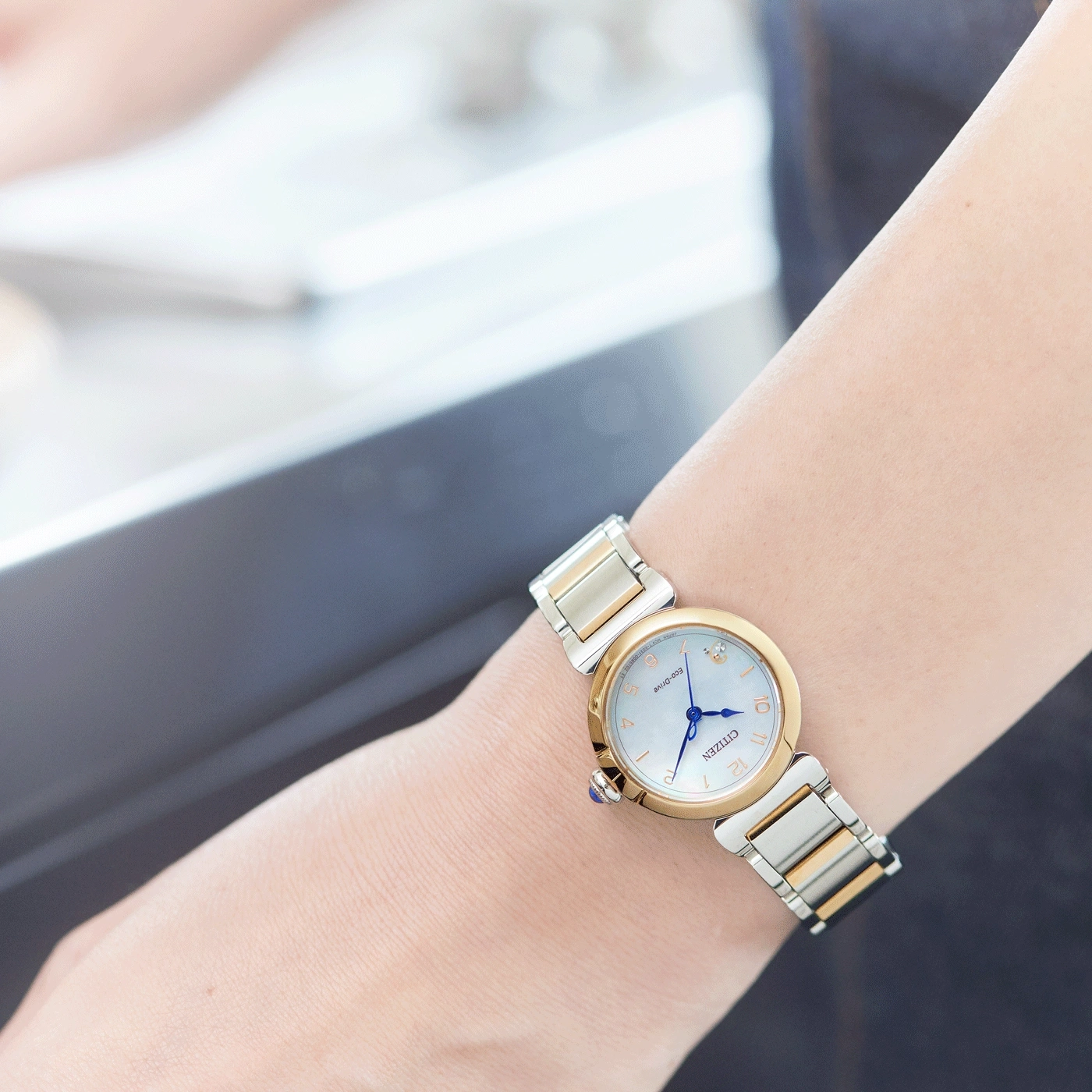 Das Handgelenk einer Frau mit einer Citizen Eco-Drive Uhr, Gold und Silber.