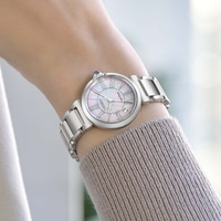 Das Handgelenk einer Frau trägt eine silberne Uhr mit einem Perlmuttzifferblatt.