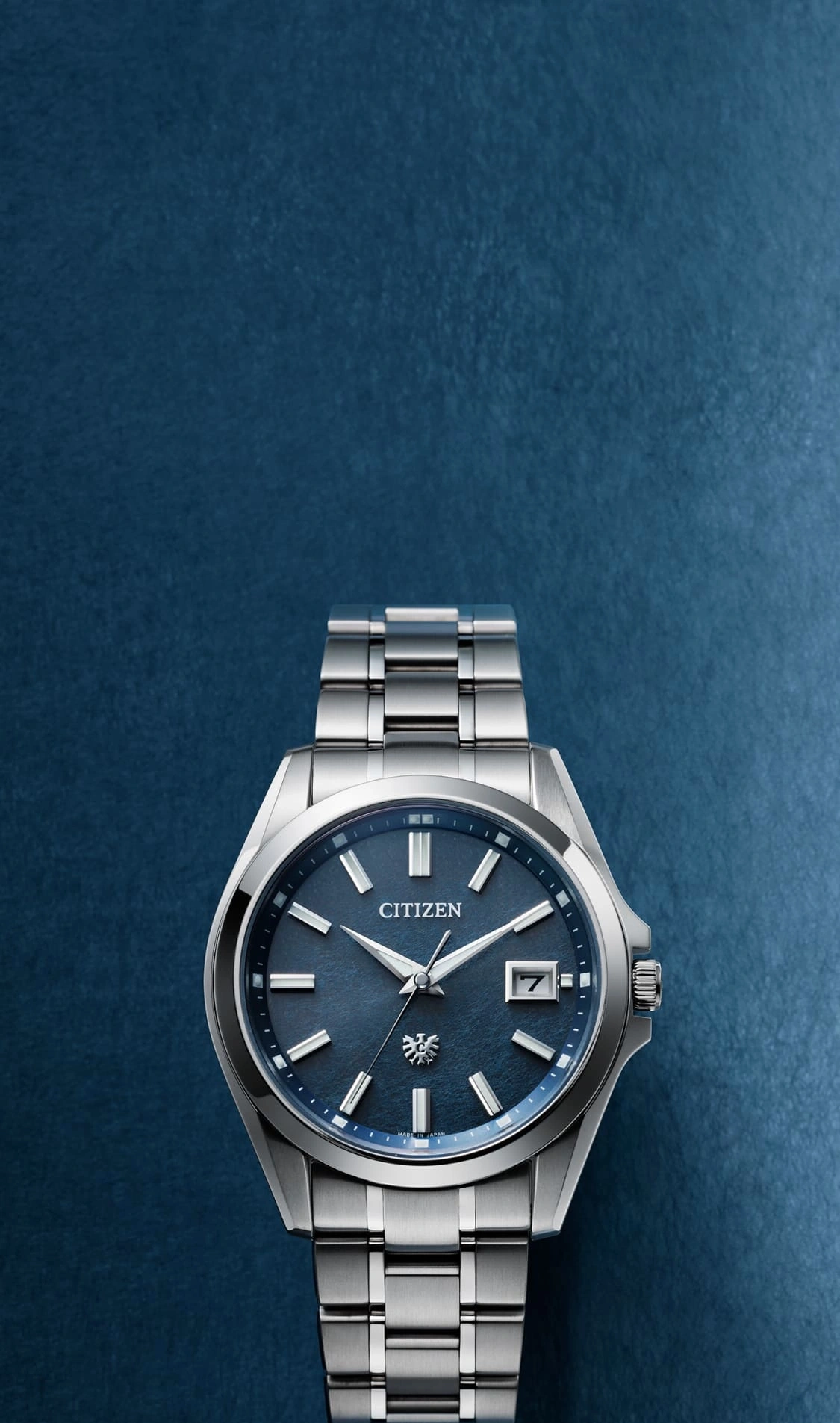 Citizen-Uhr mit blauem Zifferblatt und silbernem Armband auf blauem Hintergrund.
