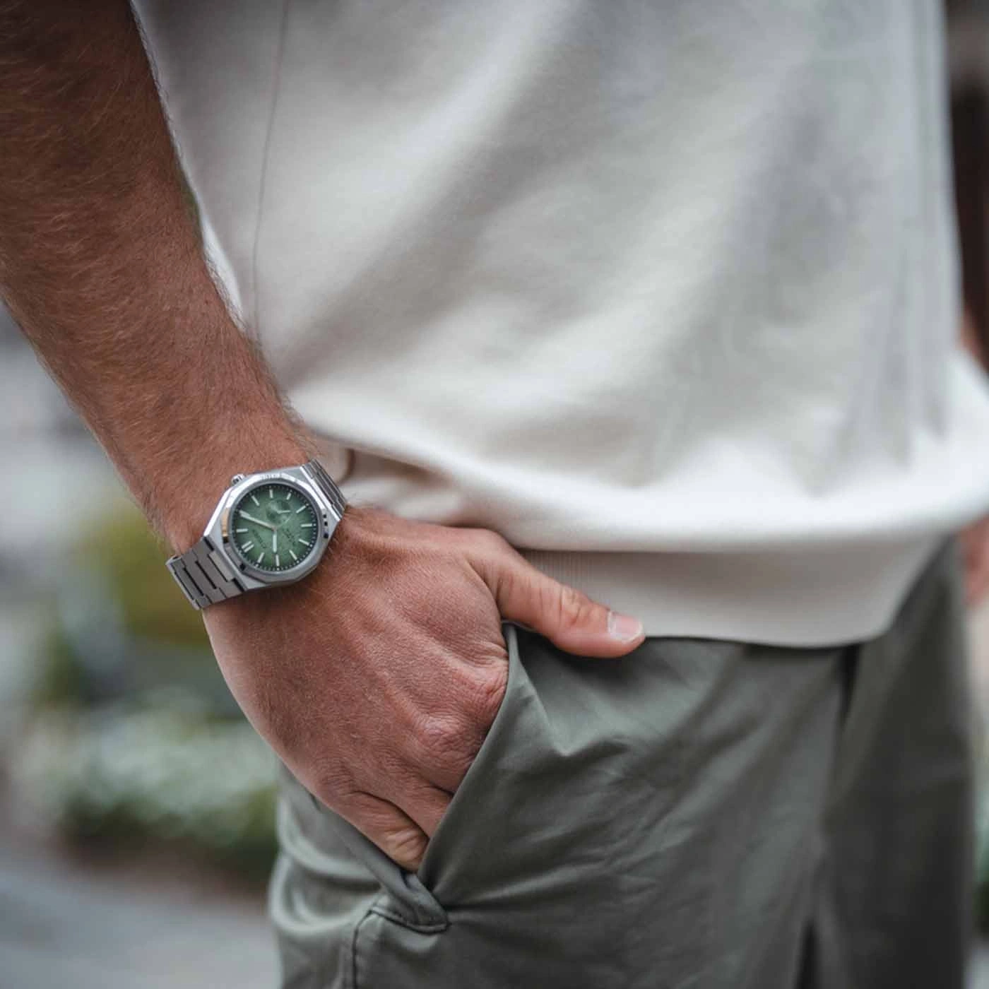 Mann trägt silberne Uhr mit grünem Zifferblatt, Hand in der Tasche.