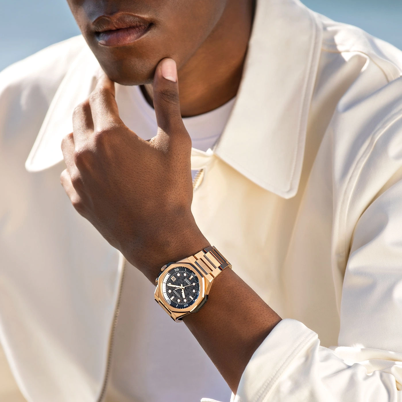 Mann mit goldener Uhr, Hand am Kinn, posiert stilvoll und elegant.