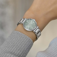Das Handgelenk einer Frau mit einer silbernen Uhr mit hellgrünem Zifferblatt.