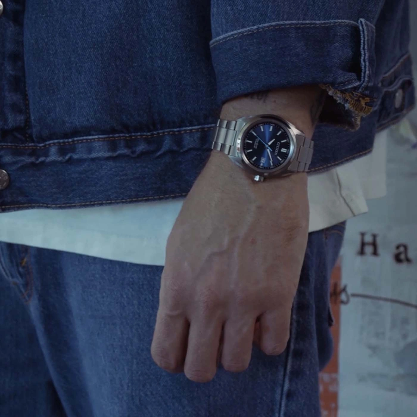 Mann trägt blaue Jeansjacke, weißes T-Shirt und Jeans mit Uhr