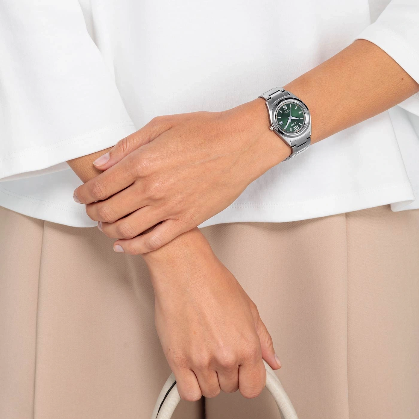 Frau mit Uhr, Handtasche, weißem Hemd und beiger Hose.