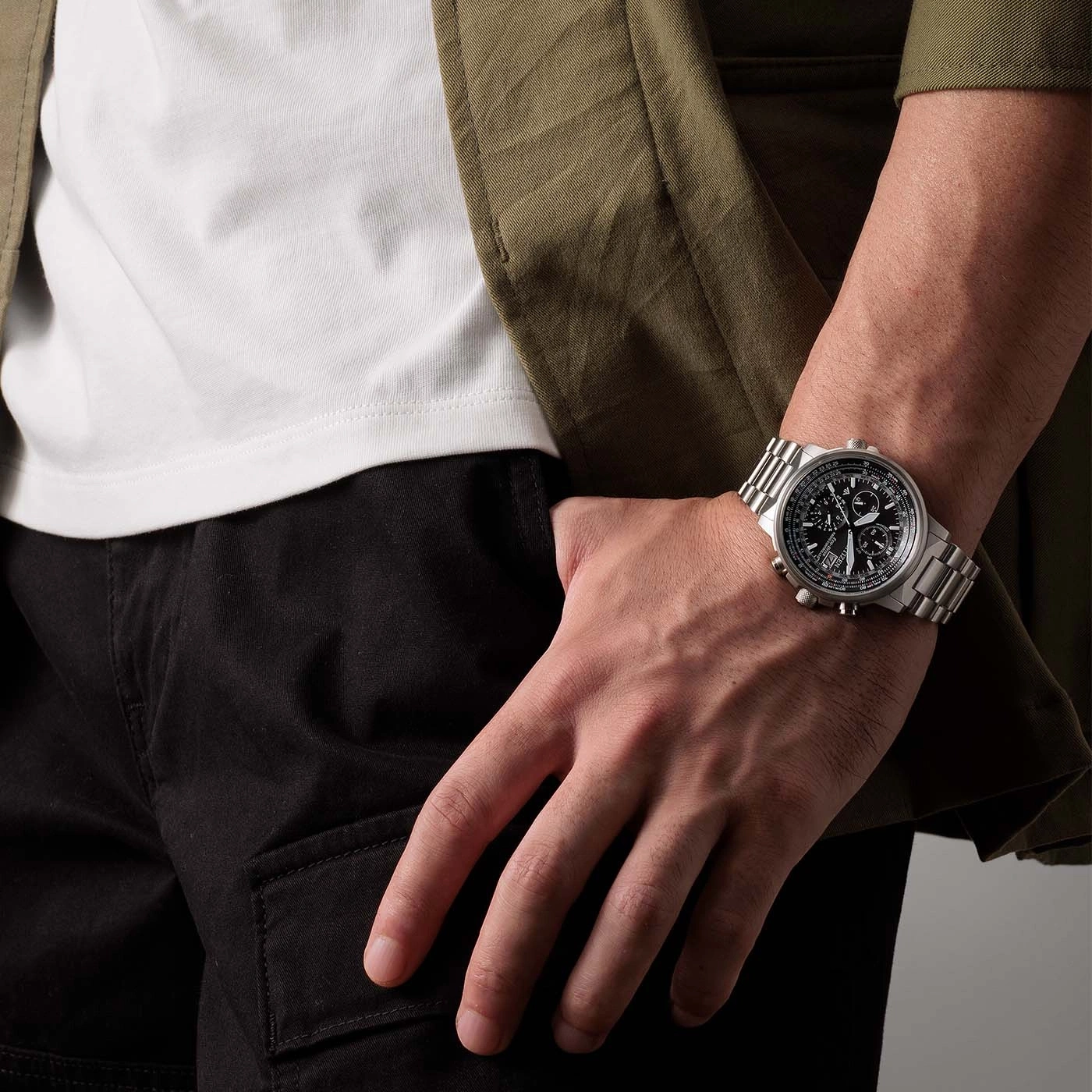 Mann mit Uhr, schwarzer Hose, weißem Hemd und grüner Jacke.