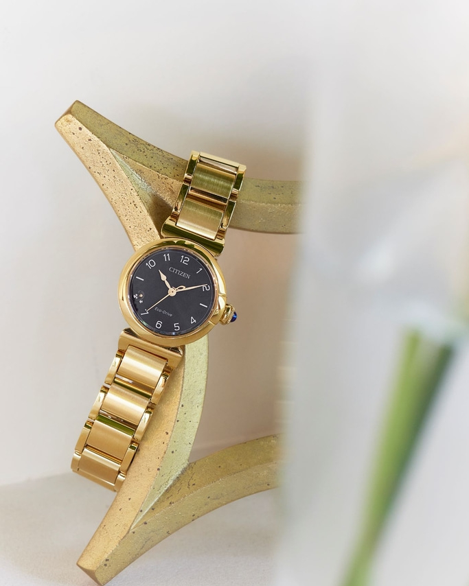 Goldene Citizen-Uhr auf goldenem Ständer mit schwarzem Zifferblatt und goldenem Armband.