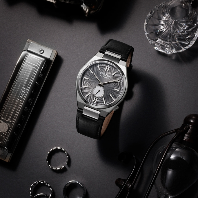 Citizen-Uhr mit schwarzem Lederarmband und Zubehör auf dunkler Oberfläche.