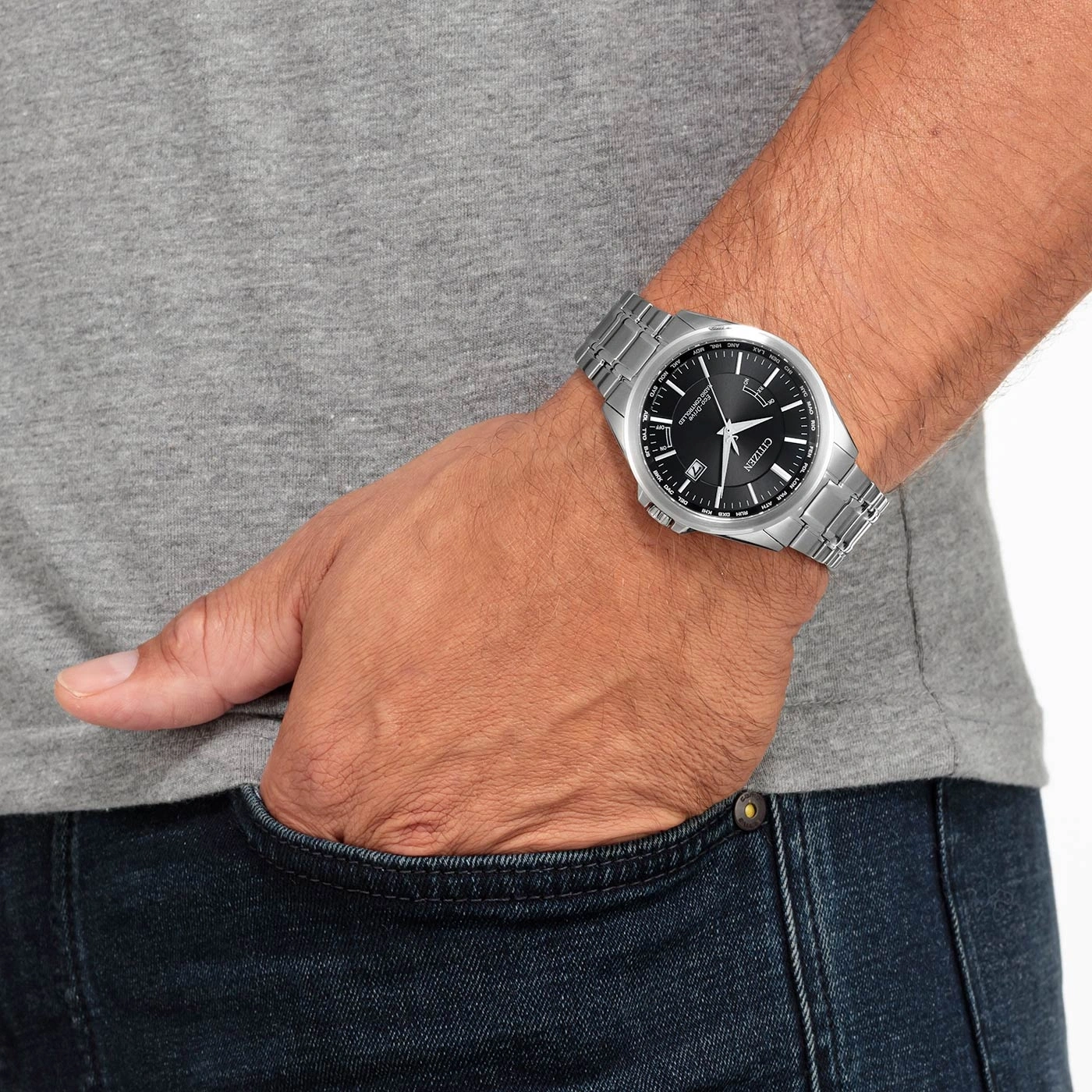 Mann mit Citizen-Uhr, Hand in der Tasche, graues Hemd, blaue Jeans.