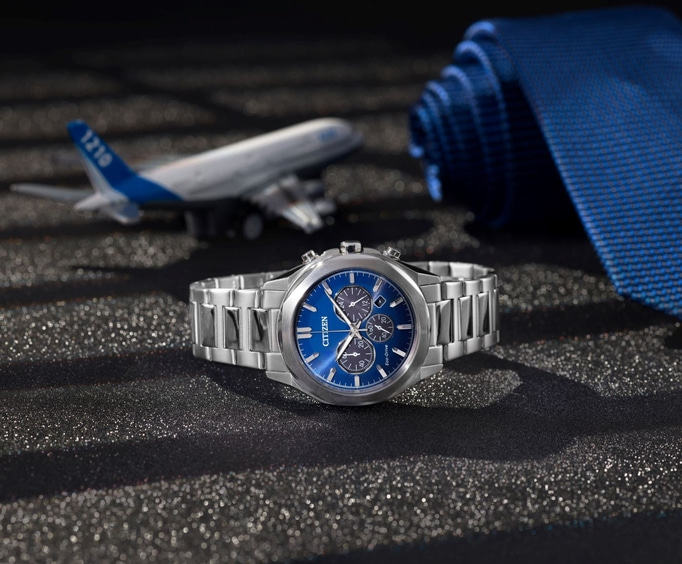 Citizen-Uhr mit blauem Zifferblatt, Flugzeug und blauer Krawatte auf schwarzem Untergrund.