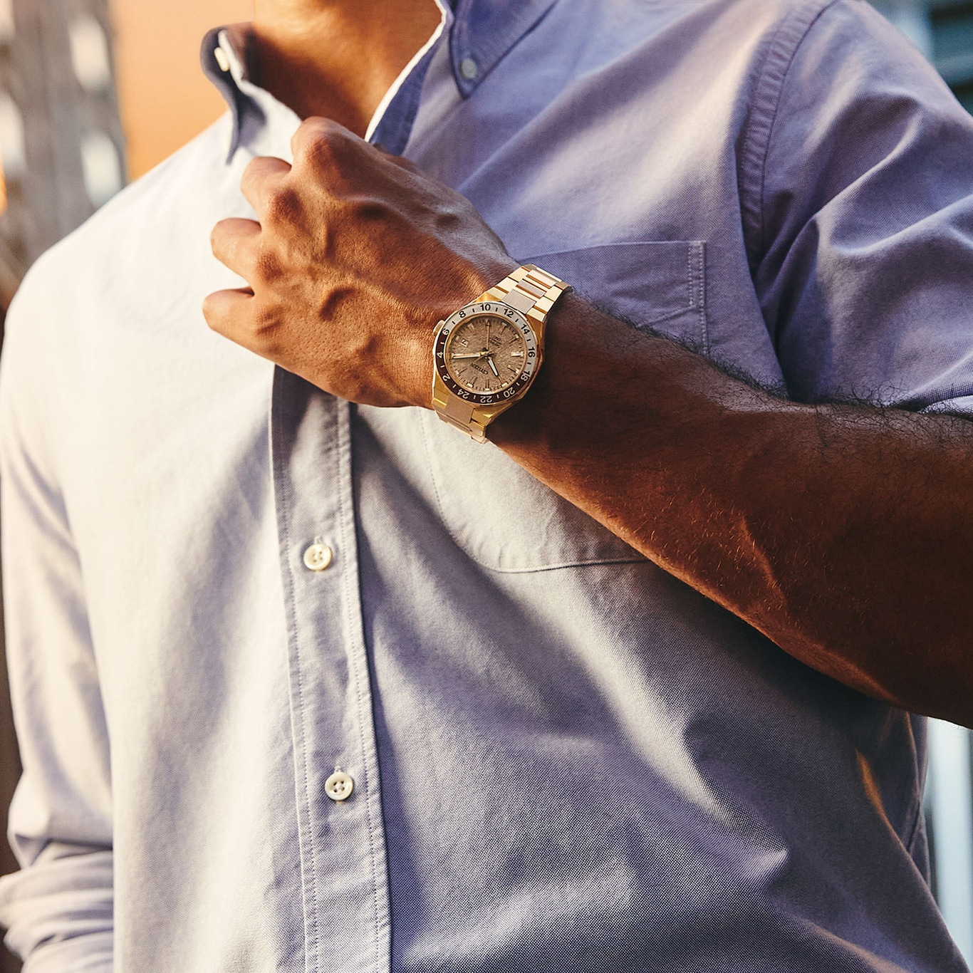 Mann mit goldener Uhr, knöpft sein hellblaues Hemd zu.