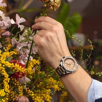 Mann mit Uhr und Blumen. Eine Person arrangiert Blumen mit einer Uhr am Handgelenk.