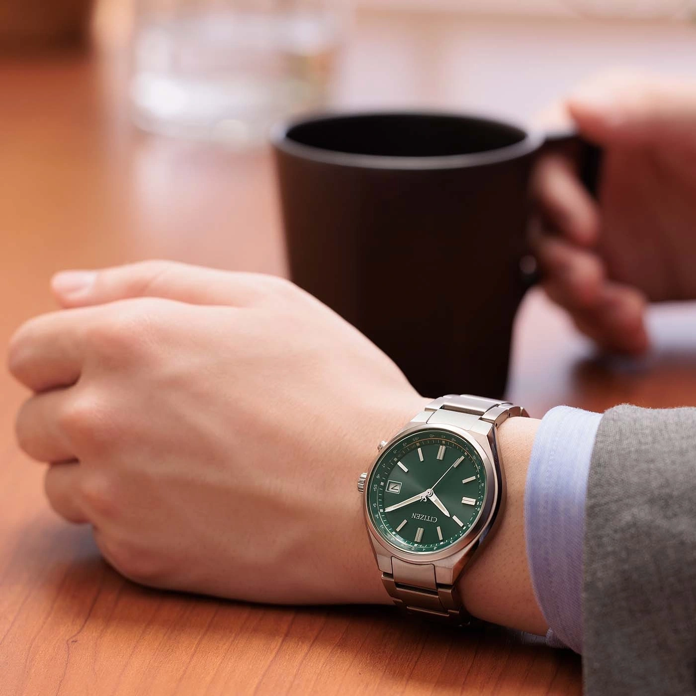 Eine Person mit einer grünen Armbanduhr und einer Kaffeetasse.