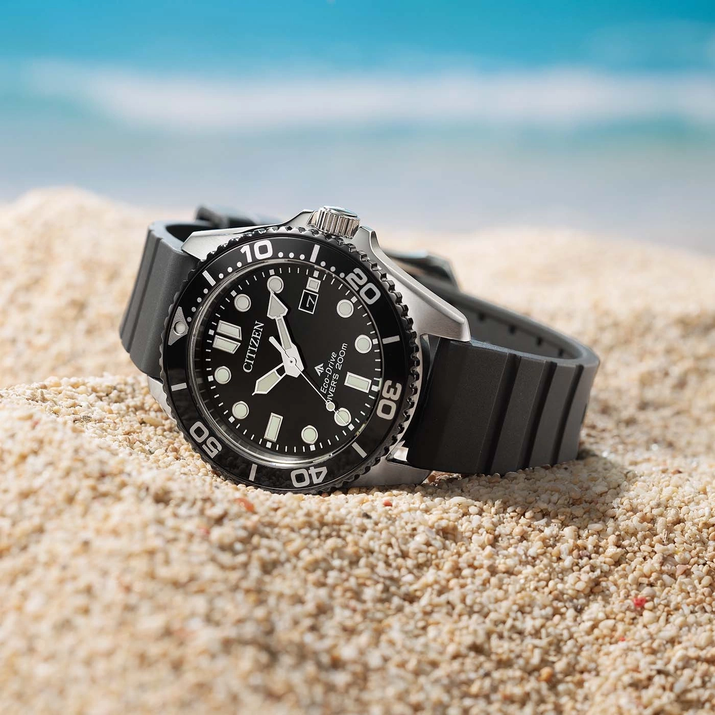 Eine schwarze Citizen Eco-Drive Taucheruhr liegt am Strand mit Ozeanhintergrund.