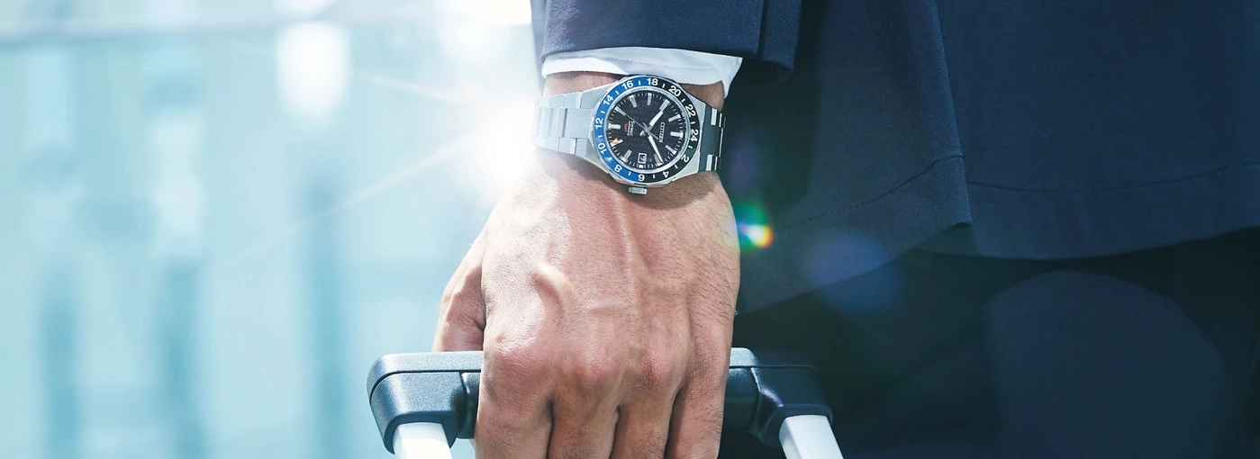 Mann mit Uhr, hält Koffer, stilvolles Reisen, Geschäftsreise, elegantes Outfit.
