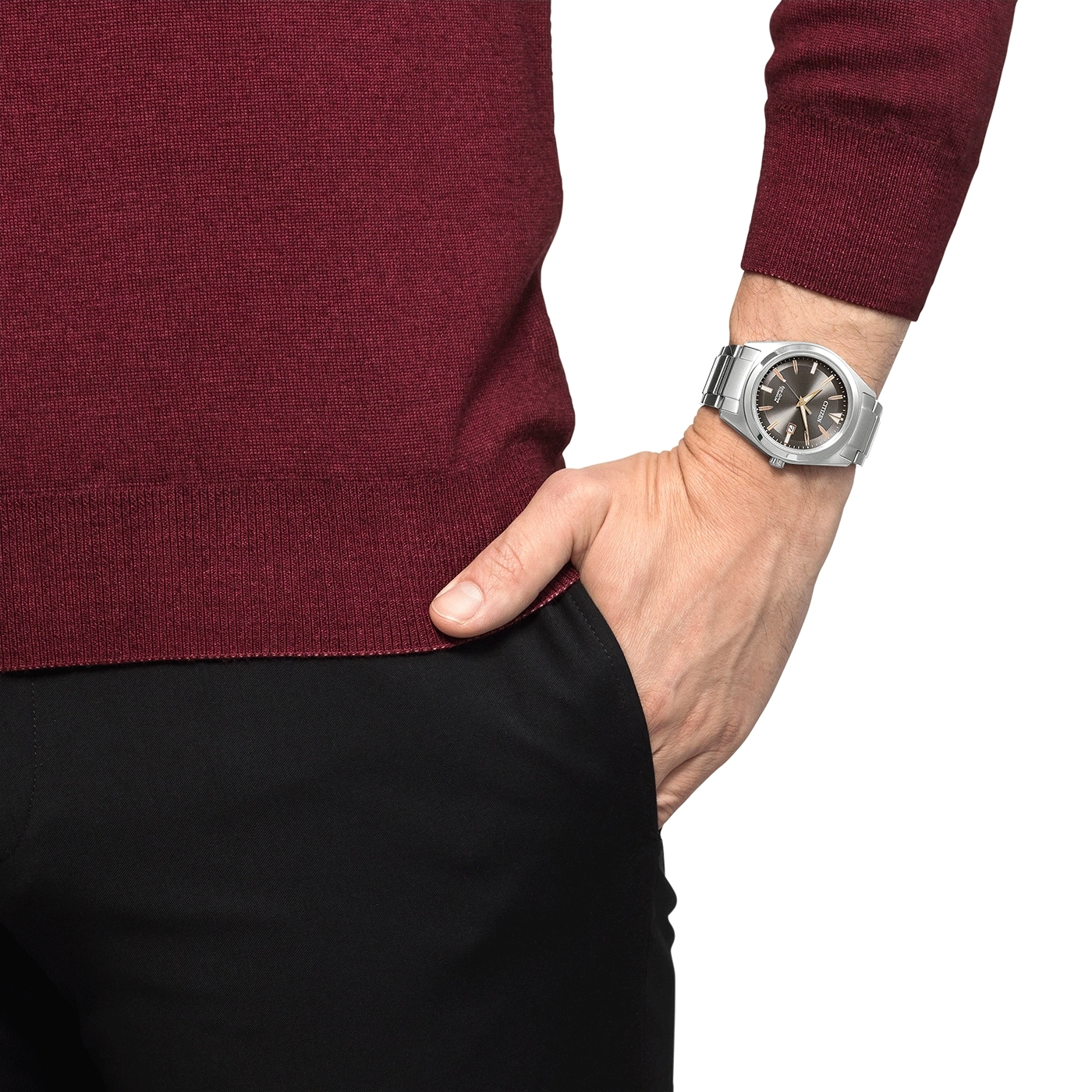 Mann mit Uhr, Hand in der Tasche, burgunderfarbener Pullover, schwarze Hose.