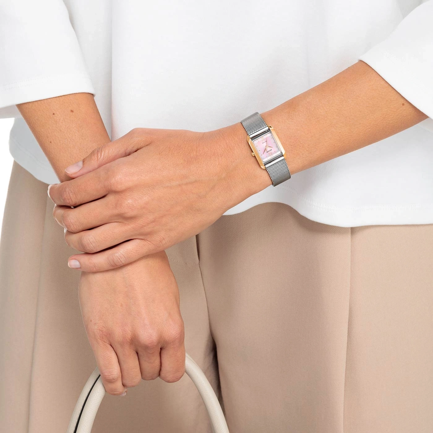 Frau mit Uhr, Handtasche, weißem Hemd und beiger Hose.