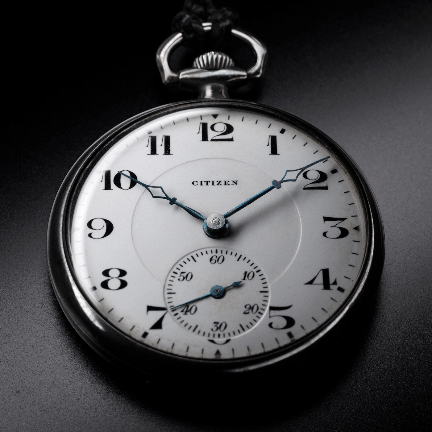 Nahaufnahme einer Citizen-Taschenuhr, die die Zeit und Details auf schwarzem Hintergrund zeigt.