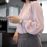 Frau in rosa Bluse und grauer Hose prüft ihre Uhr.