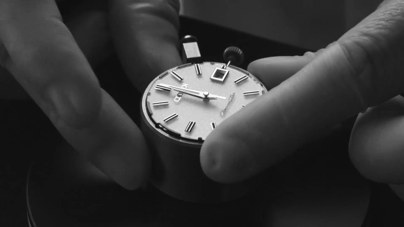 Nahaufnahme einer Uhr, die von zwei Händen gehalten wird, Zifferblatt sichtbar.