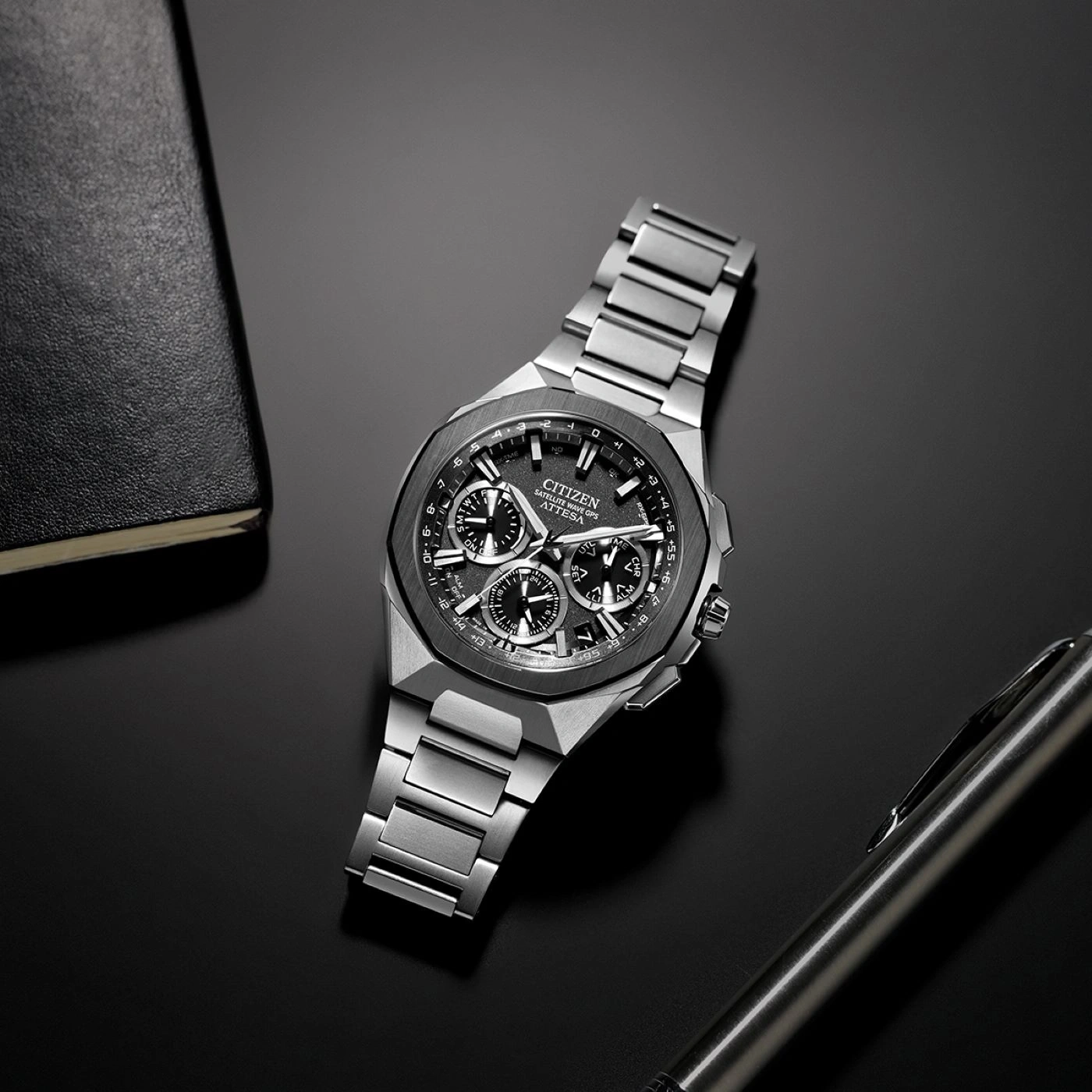 Citizen-Uhr auf schwarzer Oberfläche mit Stift und Notizbuch.