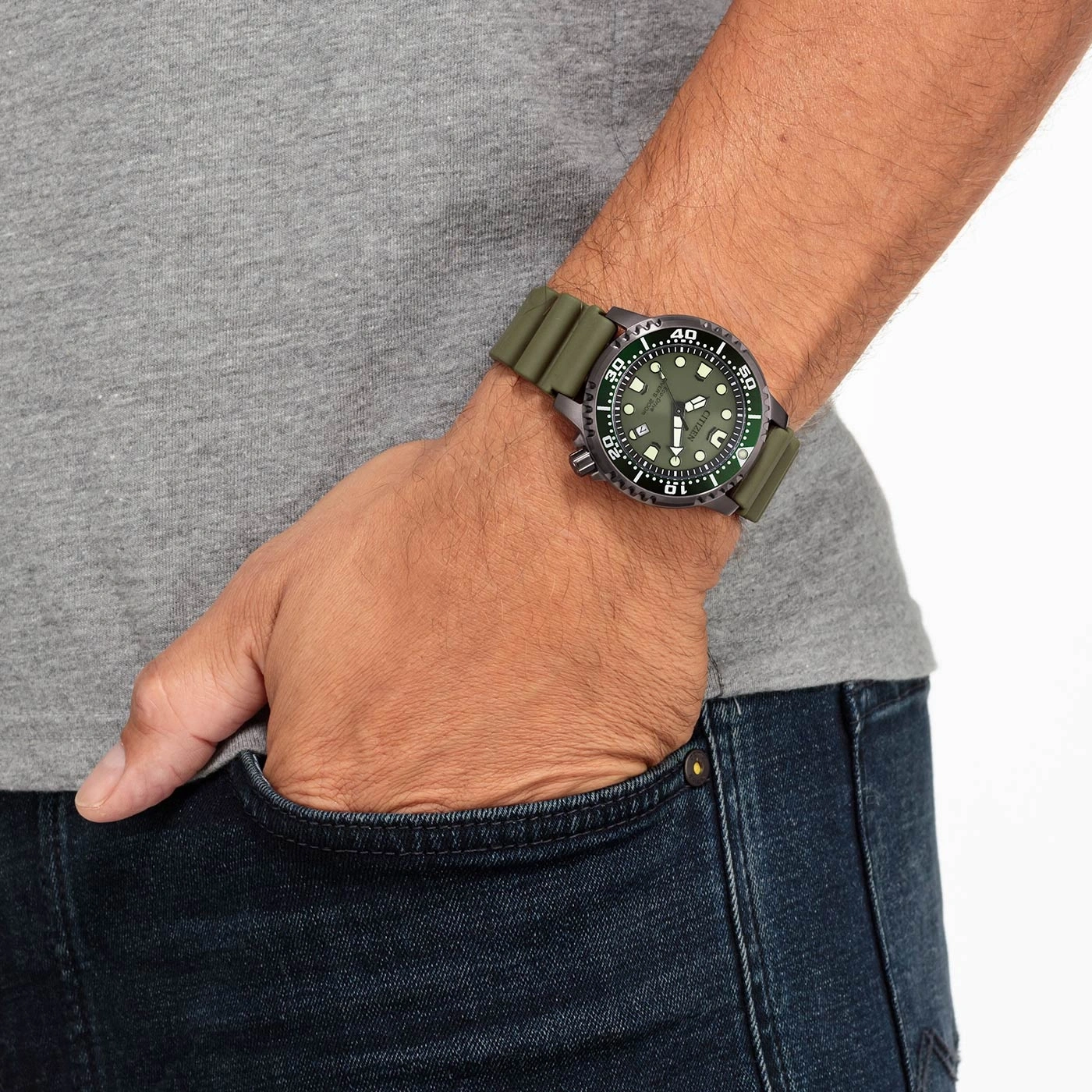 Mann mit grüner Uhr, Hand in der Tasche, graues Hemd, blaue Jeans.